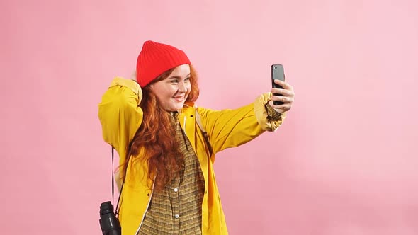 Studio Portrait of a Redheaded Happy Girl in a Yellow Raincoat Using a Smartphone