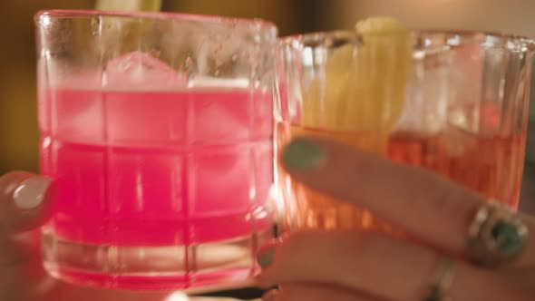 Slow motion Feminine Hands clink cocktail glasses together in sunlit bar