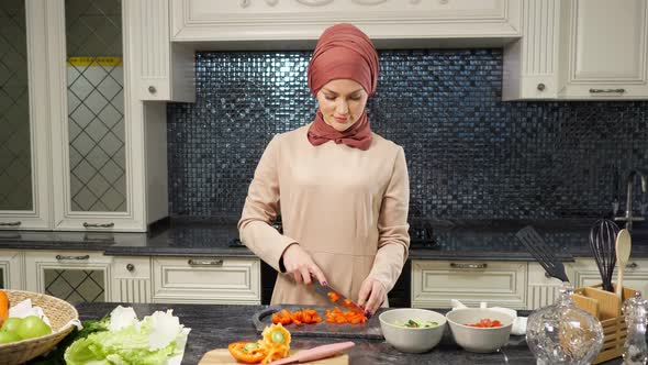 Woman in Hijab Stands at Kitchen Table Cutting Vegetable