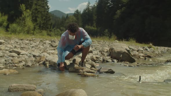 African Male Scientist in Protective Workwear Taking Water Samples From Polluted Mountain River