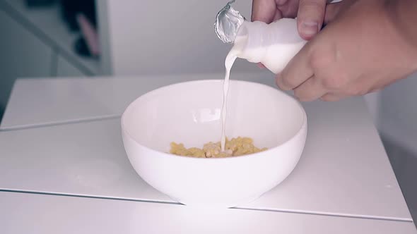Man Pours Milk From Little Bottle Into Bowl with Cereals
