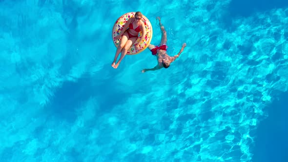 Aerial View of a Couple Having Fun in the Pool the Man Swims and the Woman Lies on an Inflatable