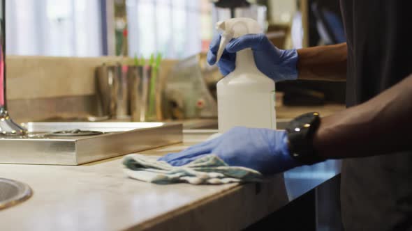 Midsection of african american male barista wearing face mask disinfecting bar surface