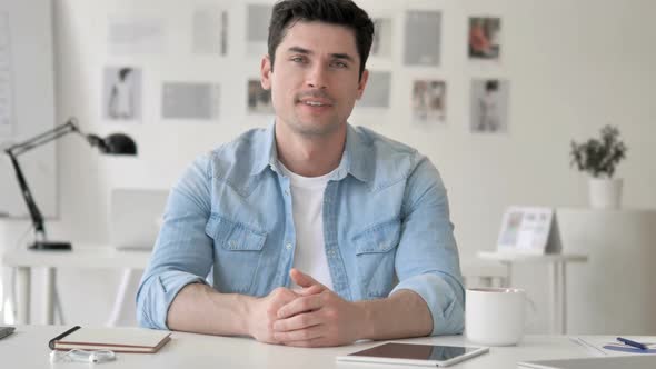 Thumbs Up By Casual Young Man Sitting at Workplace