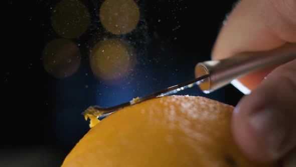 Slow motion macro shot Orange peel Spraying Citrus Oil Partlicles on Blurred Lights Background