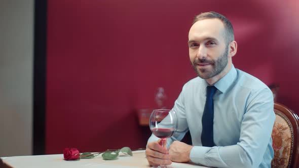 Handsome Male Sitting on Table with Bocal of Wine and Rose Waiting Female