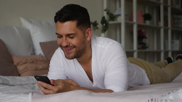 Handsome, attractive adult man, lying on the bed, typing a message to someone
