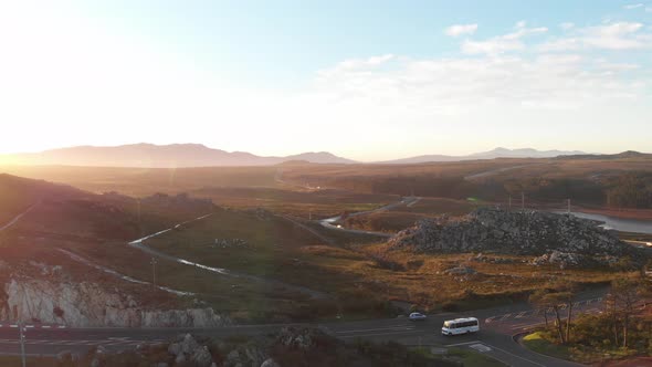 A drone shot taken of a road in a rural area in the late afternoon. The sun is setting, the sky is b