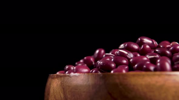Full wooden bowl of red adzuki beans on black background. Macro