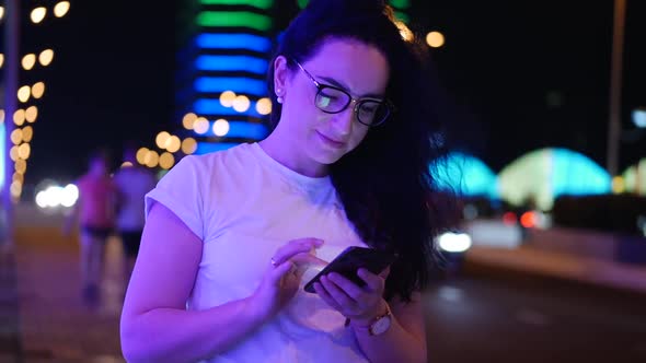 Pretty Woman Stands on the Street in a White T-shirt and Glasses, Makes Online Payments By Credit