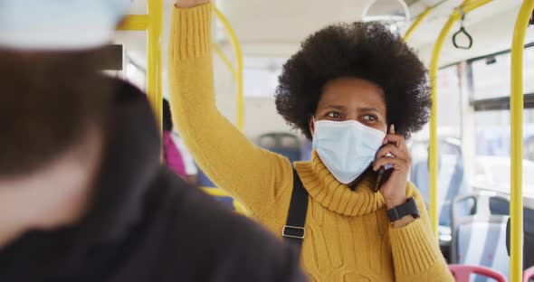 African american businesswoman with face mask talking on smartphone and standing in bus