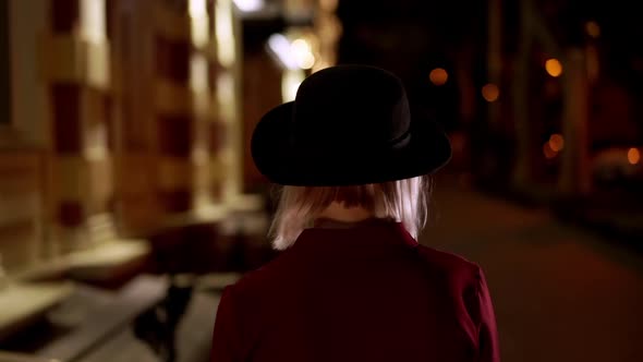 Hipster Blond Woman in Hat Turns Around with Beautiful Smile on Night City Street. Young Girl in