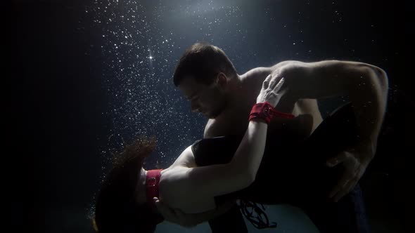 Dancing Pair Inside Water of Swimming Pool Man Is Hugging Slender Sexy Woman and Looking at Camera