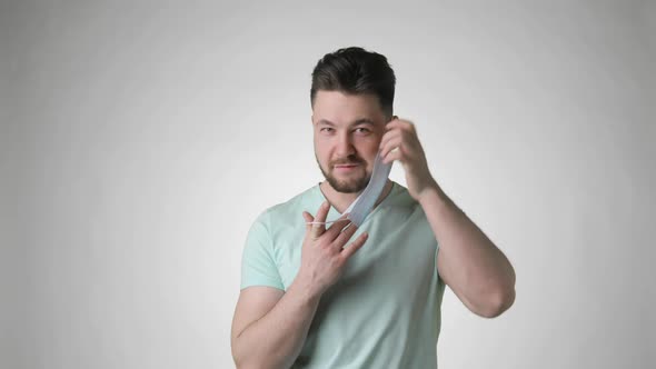 Young Bearded Man in Green Tshirt Putting on Mask on Face on Grey Background