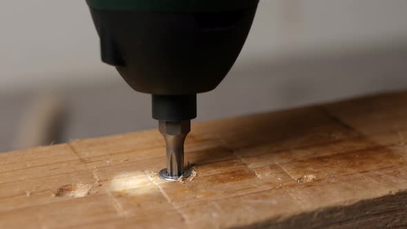 Close up unscrewing a bolt out of a wooden plank with a cordless screwdriver.