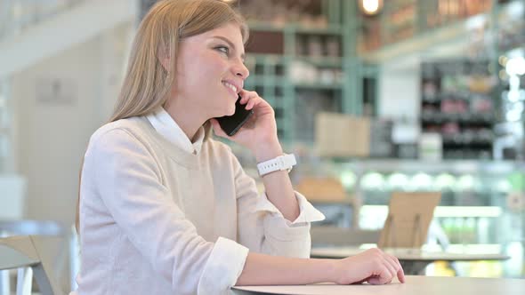 Cheerful Young Woman Talking on Smartphone in Cafe