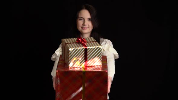 Young Woman Gives a Gift Box on Black Background. Gift Box with White Ribbon for Happy New Year