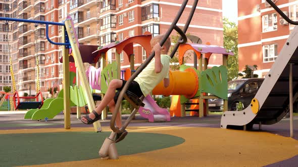 A Little Funny Boy is Spinning on an Interesting Carousel on a Modern Playground