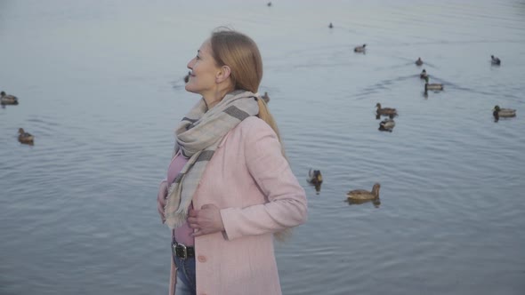 Happy Blond Caucasian Woman Turning To Camera and Smiling at the Background of Autumn River