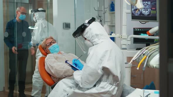 Dentist Nurse in Protective Suit Taking Notes on Clipboard