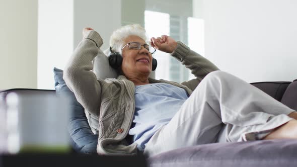 African american senior woman wearing headphones listening to music sitting on the couch at home