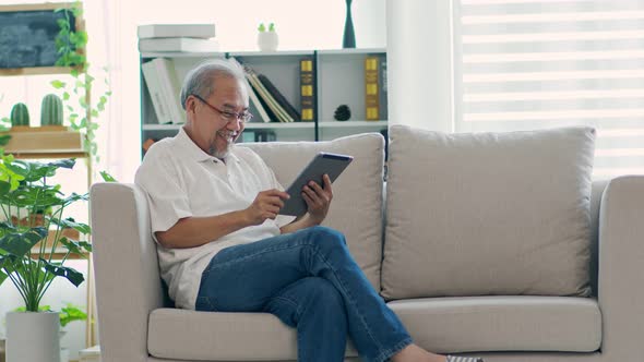 Happiness elderly asian man sitting on sofa and using computer tablet VDO Conference online