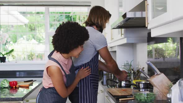 Mixed race couple wearing aprons cooking food together in the kitchen at home