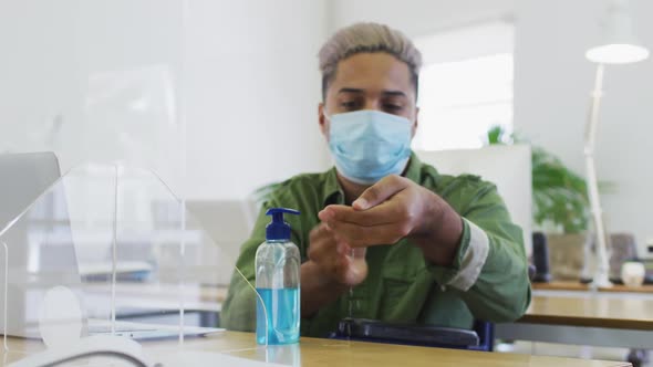 Man wearing face mask sanitizing his hands at office