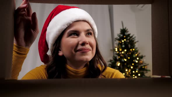 Inside Carton Box Positive Woman in Santa Claus Hat Opens Christmas Box Smiling