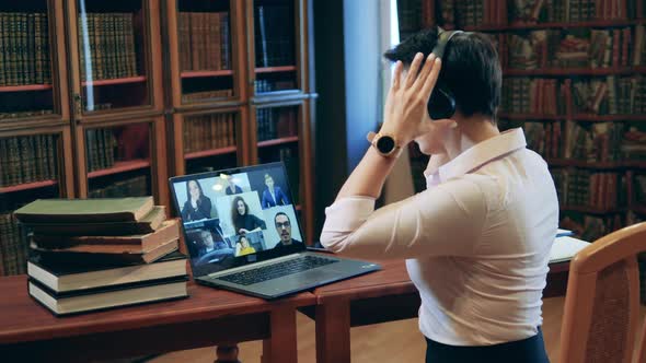 Tutor Takes Headphones on and Opens a Book Talking To Remote Students