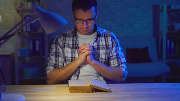 Portrait Man Sits at a Table and Reads a Prayer