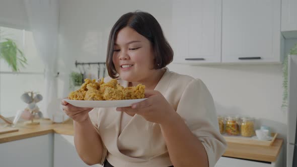 Portrait of Asian big women hold fried chicken on plate in kitchen.