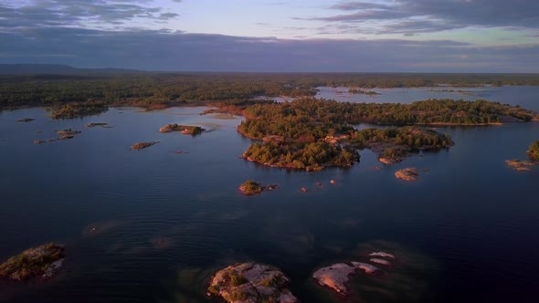 Rocky Granite Islands with Green Pine Trees in Clear Blue Lake at Sunset, Drone Aerial Wide Dolly In