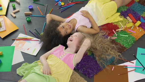 Two multiracial female children lying on carpet and laughing, happy childhood