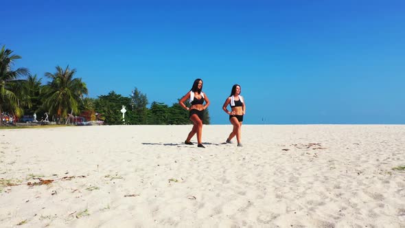 Beautiful ladies tanning on marine seashore beach break by blue green water and white sand backgroun