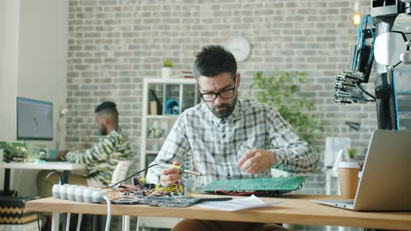 Young Specialist Making Motherboard for Robot Using Soldering Iron in Office