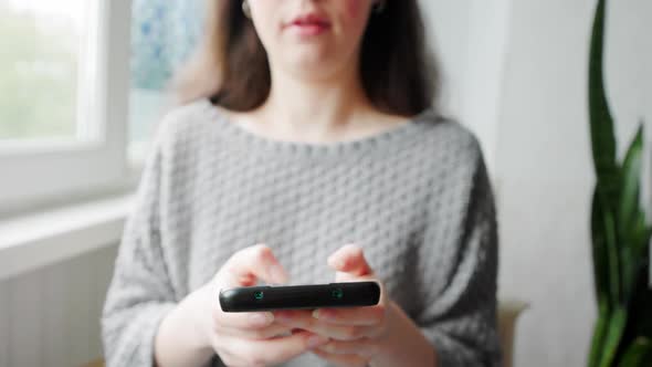 A Young Caucasian Woman in Home Clothes Texting at a Smartphone
