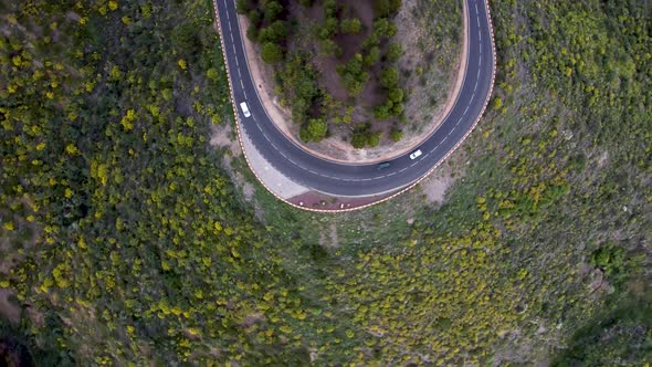 Cars driving on a mountain road turn and meeting aerial drone bird view going into clouds.