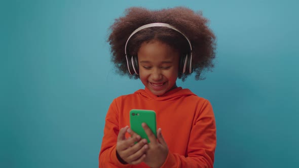 Black girl in headphones having online video call using mobile phone in hands