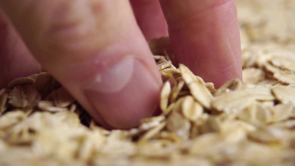 Hand takes a pinch of oat cereal flake. Falling on a heap in slow motion. Dry oatmeal porridge