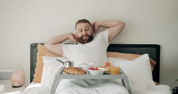 Excited Bearded Guy Stretching and Smiling While Having Breakfast in Bed, Happy Man in Good Shape