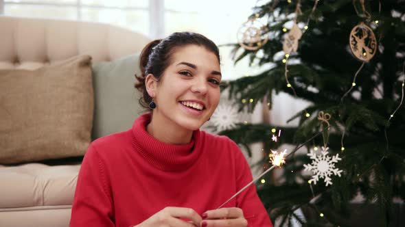 Smiling Friendly Attractive Young Woman Sitting on the Floor By the Christmas Tree Celebrating Xmas