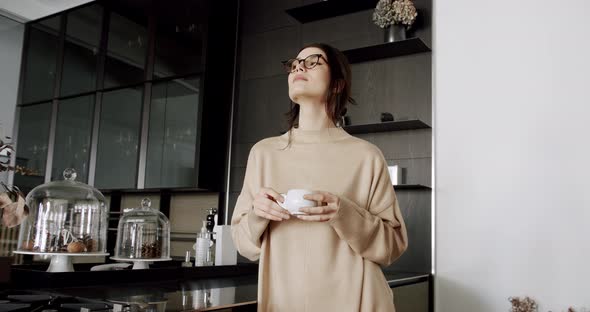 A Beautiful Young Woman is Drinking Coffee in the Modern Kitchen Room at Home