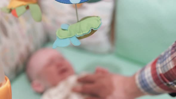 A young dad is stroking a newborn baby in a crib.