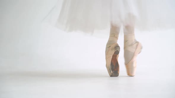 Female in a White Tutu Dance Ballet and Balancing in Pointe Shoes View of the Legs White Background