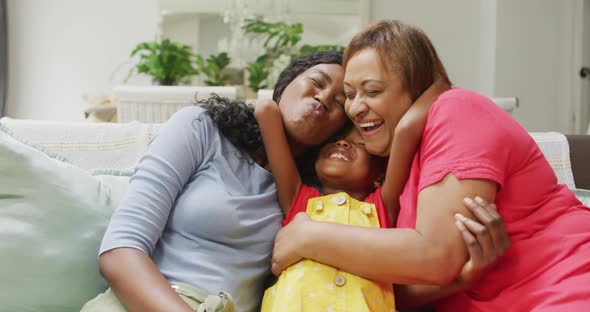 Happy african american grandmother, mother and daughter hugging on sofa