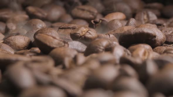 Close up slow motion shot of beans falling onto a full tray of roasting coffee beans, the impact dis
