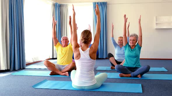 Trainer assisting senior citizens in practicing yoga