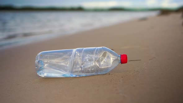 Close-up of plastic bottle on calm sandy beach being picked up by person. Water in background.