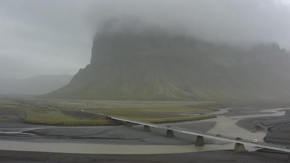 Aerial shot of a one way bridge with a mountain in the horizon on a foggy day in Iceland.